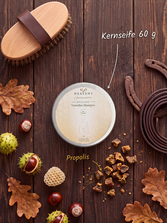 Heavens Horsecare Kernseife 60 g, festes Verwöhn-Shampoo mit Propolis in der Metalldose, auf dunklem Holz zwischen Pferdebürste, Hufeisen, Kastanien, Eichenlaub und Rohpropolis