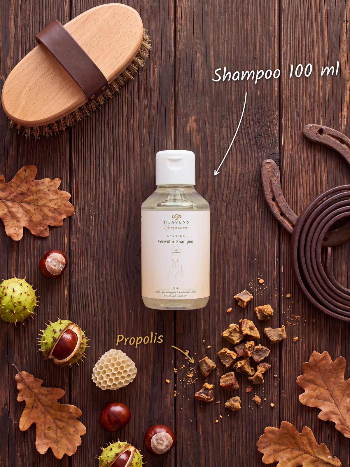 Heavens Horsecare Verwöhn-Shampoo 100 ml mit Propolis in der Flasche, auf dunklem Holz neben Pferdebürste, Hufeisen und Lederstrick, dazu Rohpropolis, eine Wabe, Kastanien und Eichenlaub