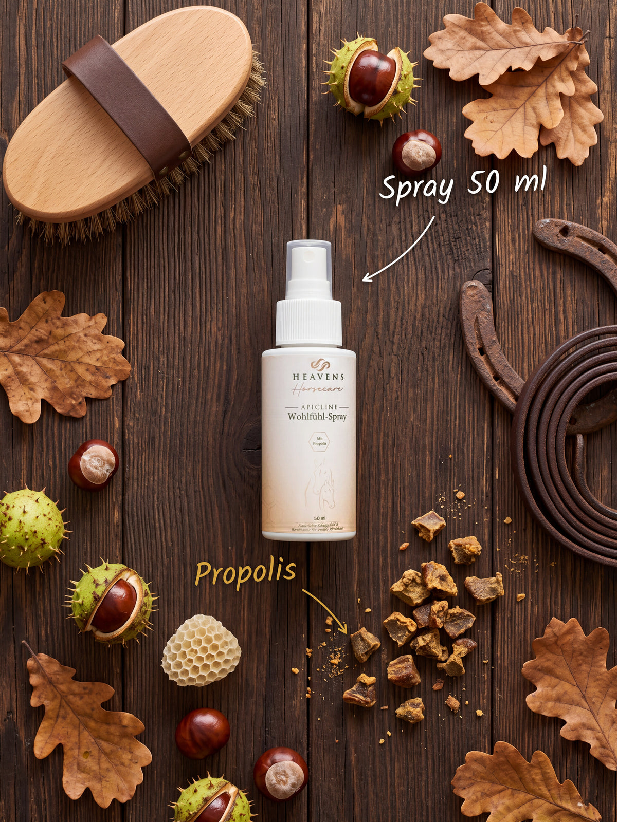 Heavens Horsecare Wohlfühl-Spray 50 ml mit Propolis in der Sprühflasche, auf dunklem Holz neben Pferdebürste, Hufeisen und Lederstrick, dazu Rohpropolis, eine Wabe, Kastanien und Eichenlaub