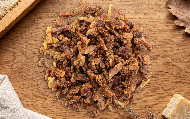 Rohpropolis in Krümeln auf einem Holzbrett, daneben eine Wabe im Rähmchen, Eichenlaub, Leinen, Bienenwachs und Heidekraut